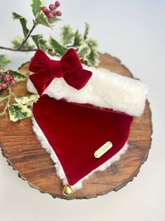 a red and white santa hat with a bow on it sitting on top of a piece of wood