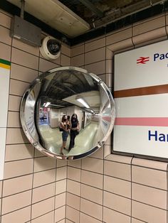 two people standing in front of a mirror on the wall next to a subway sign