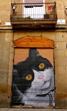 a cat painted on the side of a building with an open door and balcony above it