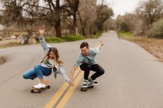 two people riding skateboards down the middle of a road with trees in the background