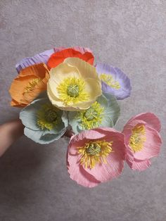 four different colored paper flowers in a person's hand on a gray background,