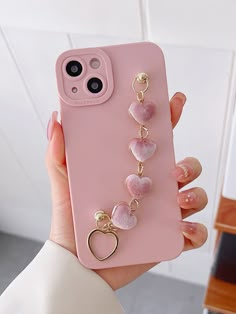 a person holding a pink phone case with heart charms attached to the back of it