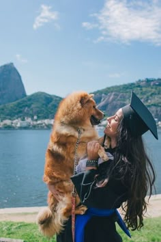 a woman holding a dog in her arms and wearing a graduation cap with mountains in the background