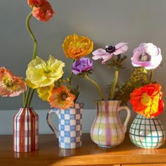 three vases with flowers in them sitting on a table next to a wall,