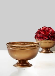 two golden bowls with flowers in them on a white table top, one is empty and the other has a red flower