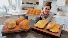 a woman sitting at a kitchen counter with breads and rolls on the cutting board