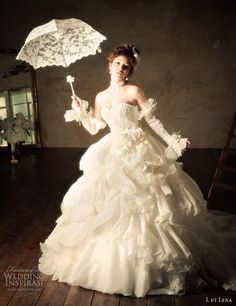 a woman in a white wedding dress holding an umbrella and posing for a photo on a wooden floor