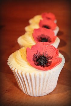 three cupcakes with red and yellow flowers on them sitting on a wooden table