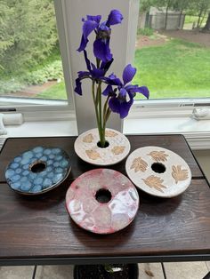 three plates with flowers and two donuts on a table near a window in front of a grassy field