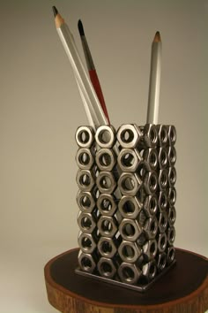 a pen holder made out of pencils and other metal objects on a wooden stand