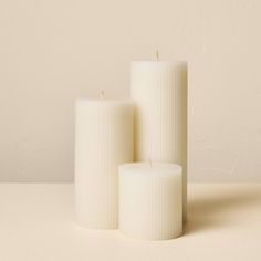 three white candles sitting next to each other on top of a beige surface with no one around them