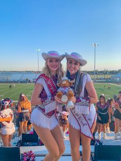 two cheerleaders pose for the camera at a football game