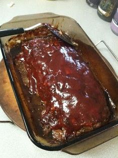 a pan filled with meat and sauce on top of a table next to utensils