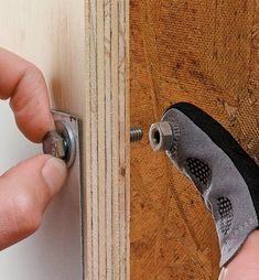 a person opening a wooden door with a screwdriver on the side and a hand holding an object in front of it