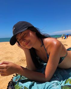 a woman laying on top of a beach next to the ocean holding a cell phone