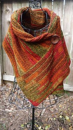 an orange and green knitted shawl sitting on top of a metal stand in front of a wooden fence