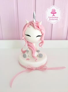 a pink and white cake with a little unicorn on it's head, sitting on top of a table