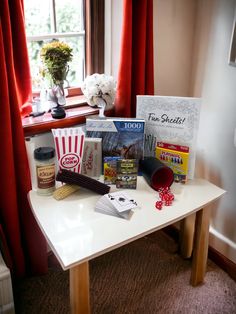 a table with books and other items on it in front of a red curtained window