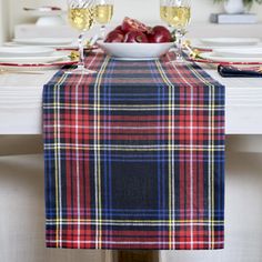 a plaid table runner with wine glasses and fruit on it in front of a white dining room table