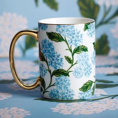 a blue and white coffee cup with green leaves on the inside is sitting on a floral tablecloth