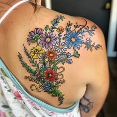 a woman's back with colorful flowers on her left shoulder and upper arm tattoo