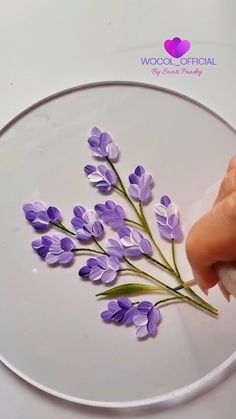 a person is cutting purple flowers on a white plate