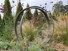 a metal sculpture in the middle of a garden with tall grass and flowers around it