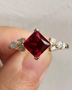 a woman's hand holding a ring with a red stone surrounded by white and yellow diamonds