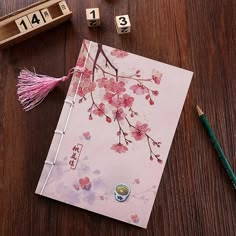 a wooden table topped with a pink notebook covered in flowers next to two dices