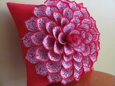 a red and white pillow with a large flower on the front sitting on a wooden table