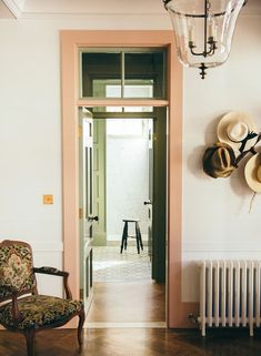 a chair sitting in front of a doorway with hats hanging on the wall