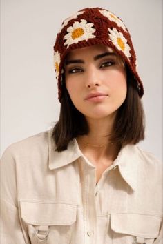 a woman wearing a crocheted hat with flowers on the front and sides, looking at the camera