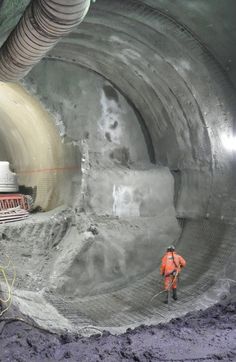 a man in an orange safety vest standing next to a large pipe