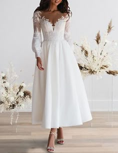 a woman in a white dress standing on a wooden floor with flowers and branches behind her