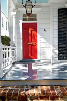 a red front door on a white house with black shutters and an iron lantern