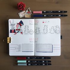 an open notebook with some markers and pens on it next to a rose, pencils, and other items