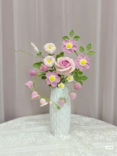 a crocheted vase filled with pink and white flowers on top of a table