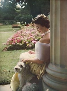 a woman in a dress sitting on a pillar with her dog next to her and looking at the ground