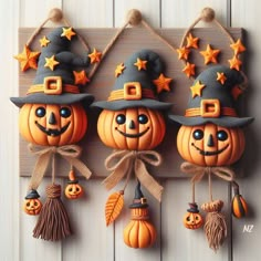 three pumpkins with hats and stars hanging on a wooden plaque, decorated with twine