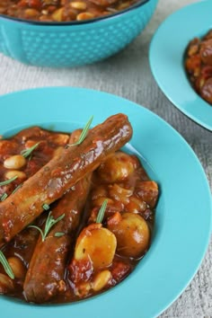 two blue plates filled with sausages and beans on top of a white tablecloth