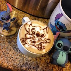 a cup of coffee with an image of stitch and stitch on it next to two small figurines