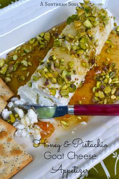 a white plate topped with cheese and nuts next to crackers on top of a table