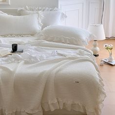 a bed with white sheets and pillows on top of it next to a table lamp