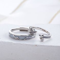 two silver rings sitting on top of a white table next to each other, one with a diamond in the middle