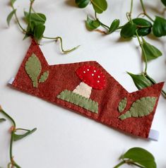 a red piece of fabric with a mushroom on it sitting next to green leaves and vines