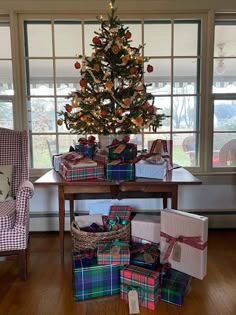 a christmas tree with presents under it in front of a table full of wrapped presents