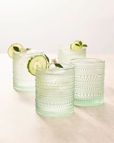 three glasses with cucumbers and limes in them sitting on a counter top