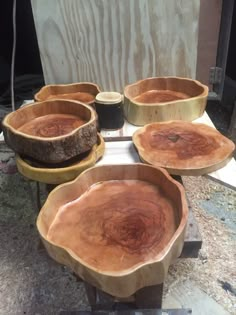 four wooden bowls sitting on top of a table next to some wood slices and plywood