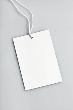 a white tag hanging from a string on top of a gray surface with an empty piece of paper attached to it