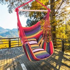 a colorful striped hammock chair hanging from a tree on a wooden deck with mountains in the background